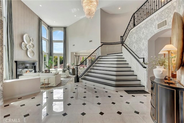 entryway featuring visible vents, a towering ceiling, arched walkways, an inviting chandelier, and stairs