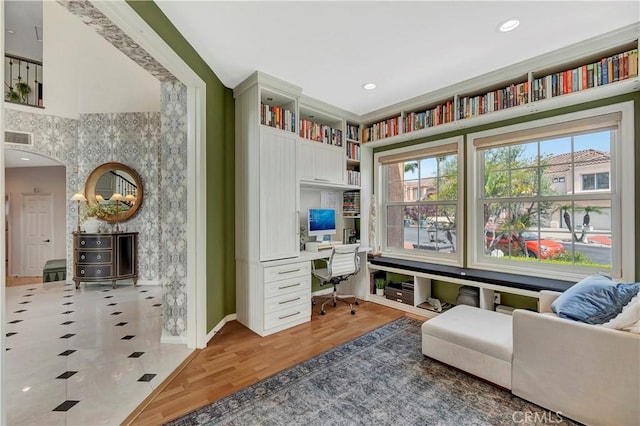 home office featuring built in study area, baseboards, light wood finished floors, and visible vents