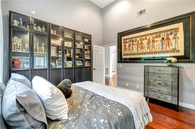 bedroom featuring baseboards, a high ceiling, wood finished floors, and visible vents