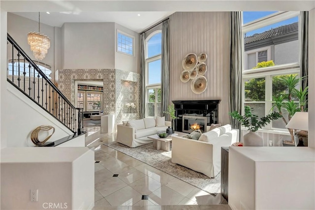 tiled living room featuring a glass covered fireplace, a high ceiling, stairs, and a notable chandelier