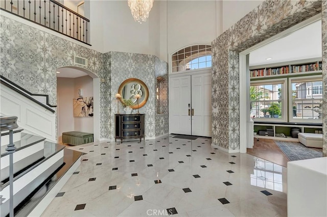 entrance foyer featuring a high ceiling, an inviting chandelier, arched walkways, baseboards, and visible vents
