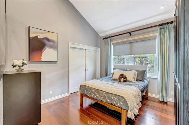 bedroom with a closet, baseboards, high vaulted ceiling, and hardwood / wood-style floors