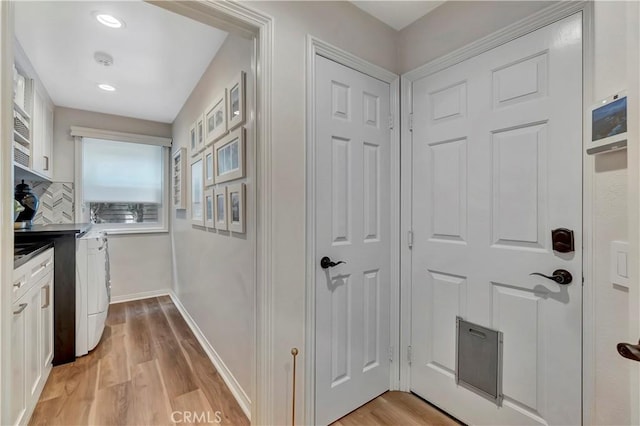interior space featuring decorative backsplash, white cabinets, light wood finished floors, and washer / clothes dryer
