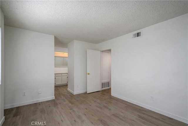 unfurnished bedroom with baseboards, a textured ceiling, visible vents, and wood finished floors