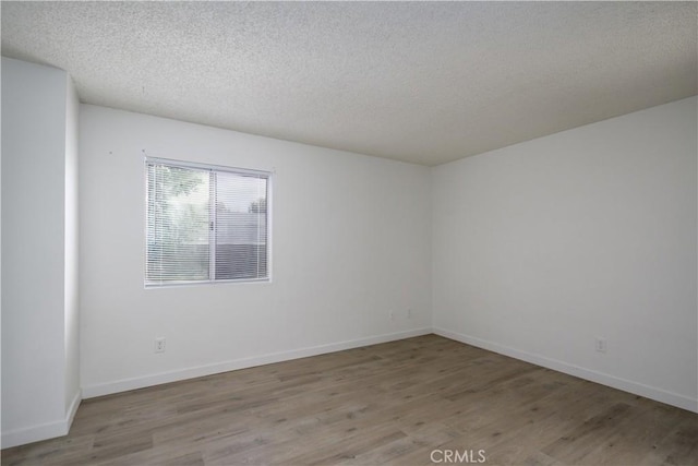 empty room featuring a textured ceiling, baseboards, and wood finished floors