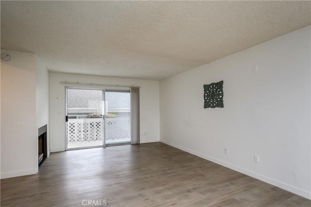 spare room featuring baseboards, a textured ceiling, a glass covered fireplace, and wood finished floors