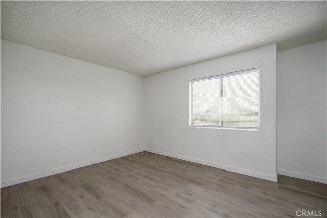 spare room featuring baseboards, a textured ceiling, and wood finished floors