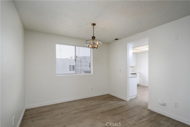 empty room featuring an inviting chandelier, visible vents, wood finished floors, baseboards, and a textured ceiling