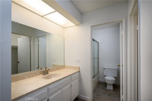 full bath with vanity, shower / bath combination with glass door, wood finished floors, and toilet