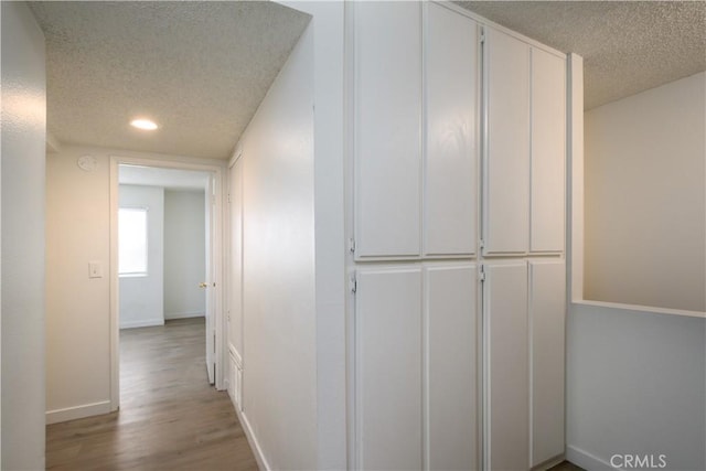 corridor with baseboards, recessed lighting, a textured ceiling, and wood finished floors