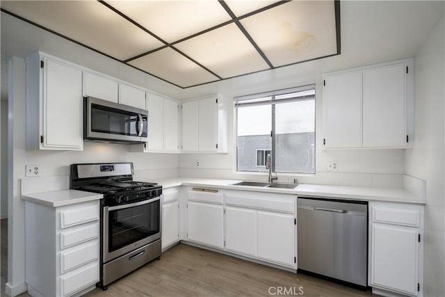 kitchen featuring stainless steel appliances, white cabinetry, a sink, and light wood-style floors