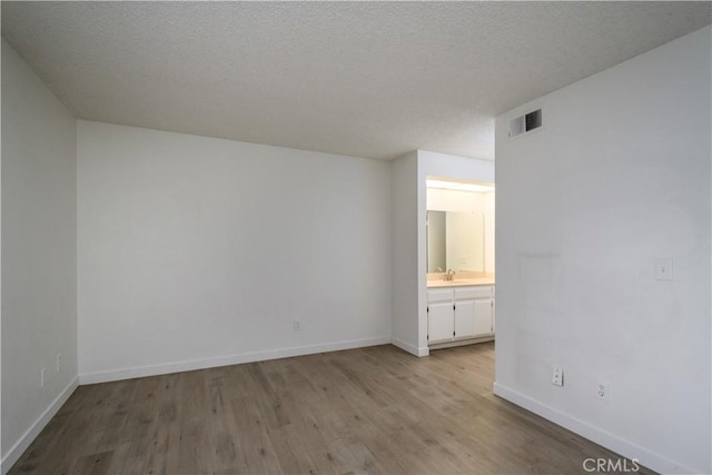 spare room featuring a textured ceiling, baseboards, visible vents, and wood finished floors
