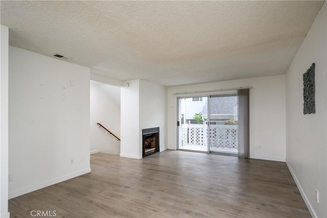 unfurnished living room with visible vents, wood finished floors, a fireplace, baseboards, and a textured ceiling