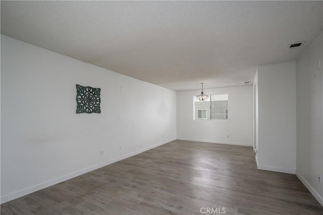 empty room featuring an inviting chandelier, baseboards, and wood finished floors