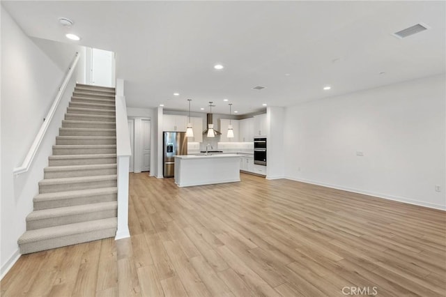 unfurnished living room with light wood-style flooring, stairs, recessed lighting, baseboards, and visible vents