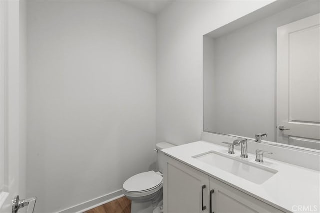 half bath with vanity, baseboards, toilet, and wood finished floors