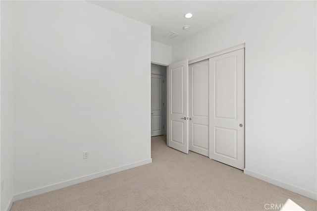 unfurnished bedroom featuring light colored carpet, baseboards, visible vents, and a closet