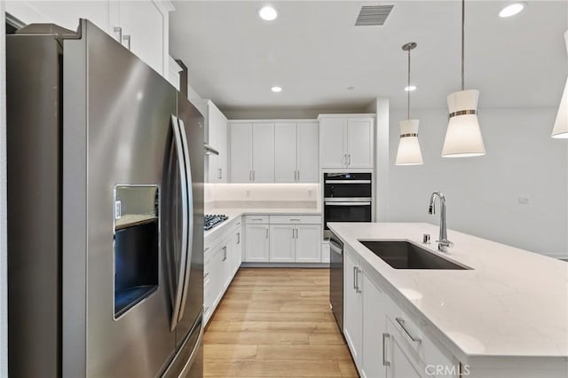 kitchen featuring appliances with stainless steel finishes, a sink, light stone counters, white cabinets, and light wood-style floors