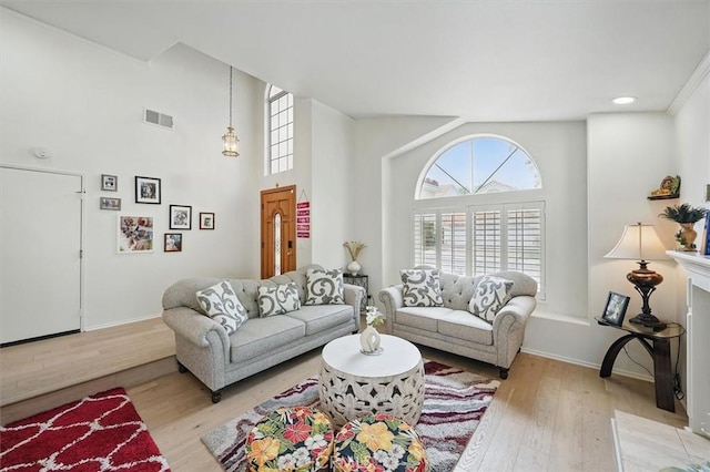 living room with visible vents, light wood-style flooring, a towering ceiling, and a wealth of natural light
