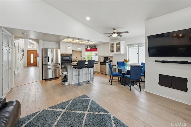 living area featuring light wood-type flooring, arched walkways, a ceiling fan, and vaulted ceiling