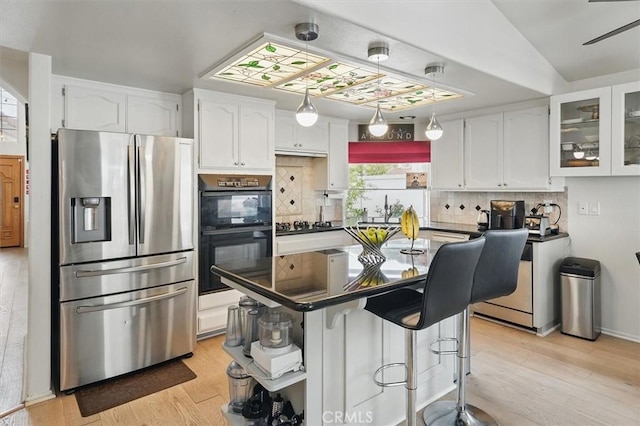 kitchen featuring white cabinets, light wood finished floors, black appliances, and tasteful backsplash