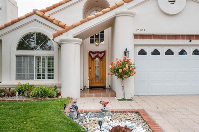 view of exterior entry featuring a garage, stucco siding, a lawn, and driveway