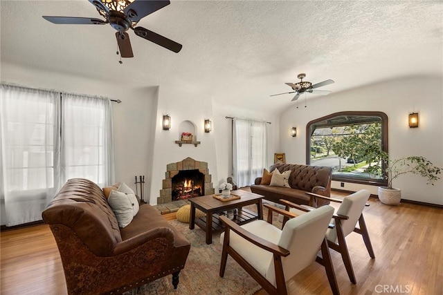 living area with a warm lit fireplace, a textured ceiling, ceiling fan, and wood finished floors