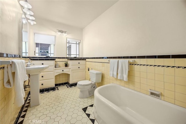 full bathroom with a tub to relax in, a wainscoted wall, toilet, and tile walls
