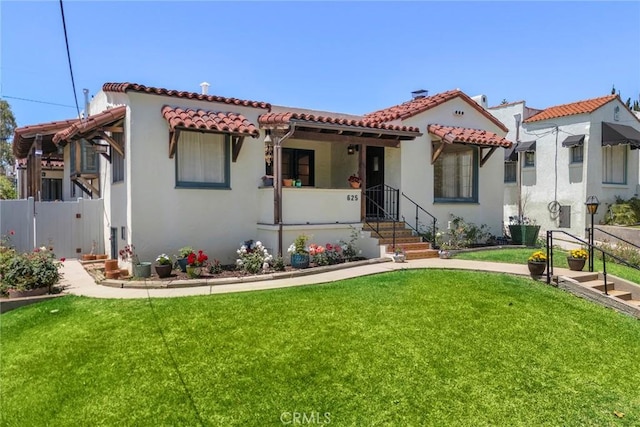 mediterranean / spanish-style home featuring a front lawn, stucco siding, a tile roof, and fence
