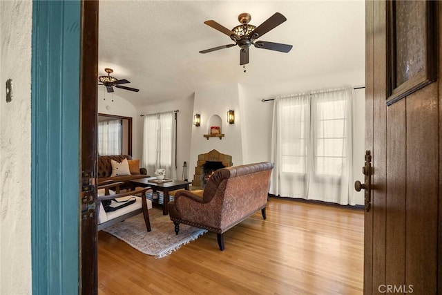 living room featuring light wood-type flooring, a ceiling fan, a healthy amount of sunlight, and a stone fireplace