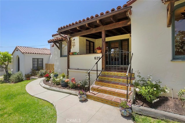 view of exterior entry with a lawn, stucco siding, and a tile roof