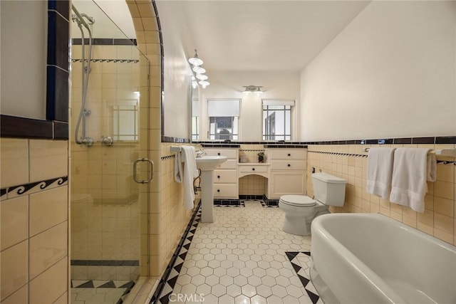 bathroom with a bathtub, tile walls, a stall shower, a wainscoted wall, and toilet