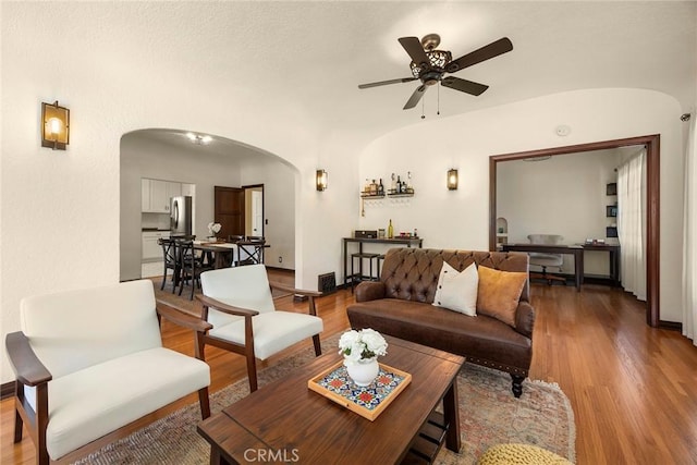 living room with baseboards, arched walkways, a ceiling fan, and wood finished floors