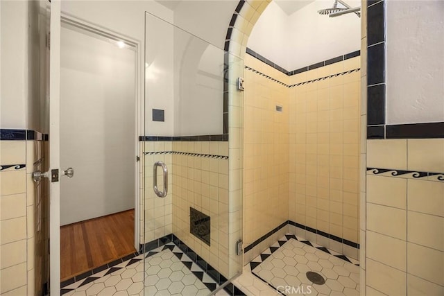 full bath featuring wainscoting, tile walls, a shower stall, and wood finished floors