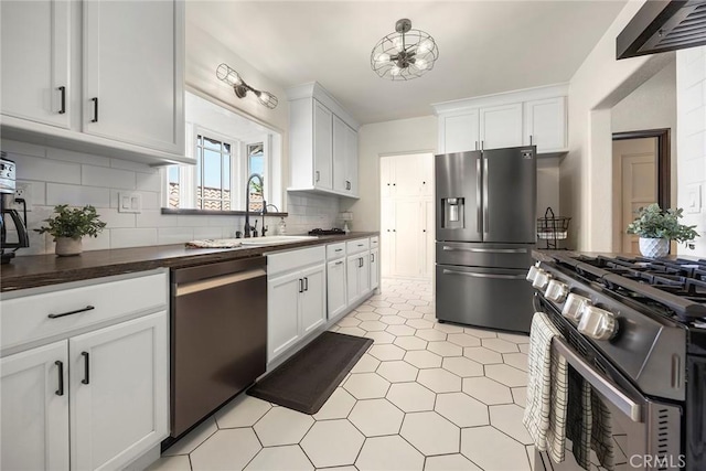 kitchen with dark countertops, tasteful backsplash, a sink, white cabinets, and stainless steel appliances