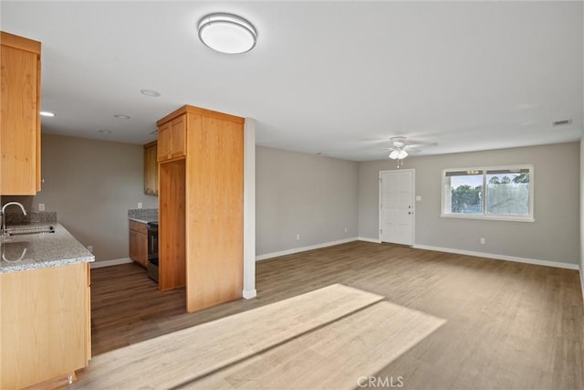 unfurnished living room with ceiling fan, a sink, baseboards, wood finished floors, and visible vents