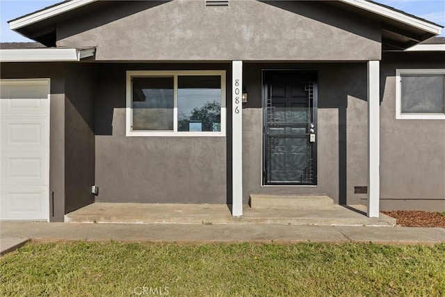 entrance to property featuring a porch, a garage, and stucco siding