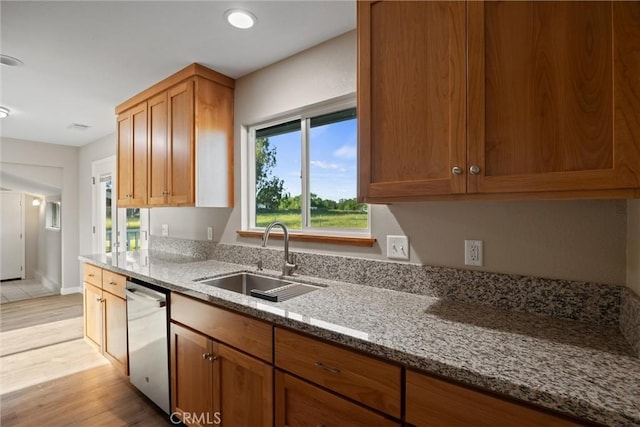 kitchen with stainless steel dishwasher, light stone countertops, light wood-style floors, brown cabinets, and a sink
