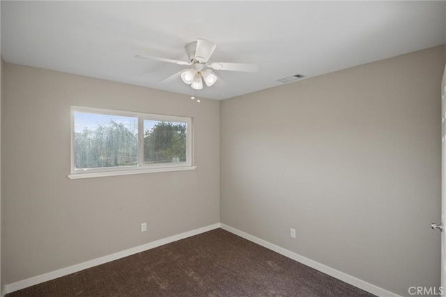 spare room with ceiling fan, visible vents, baseboards, and dark colored carpet