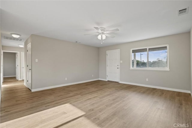 empty room with ceiling fan, visible vents, baseboards, and wood finished floors