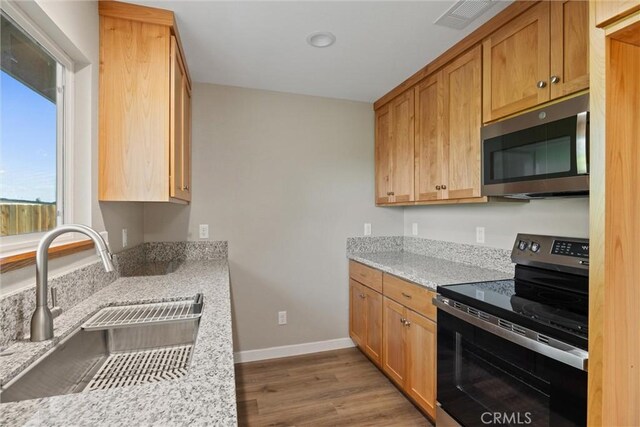 kitchen with a sink, stainless steel appliances, baseboards, wood finished floors, and visible vents