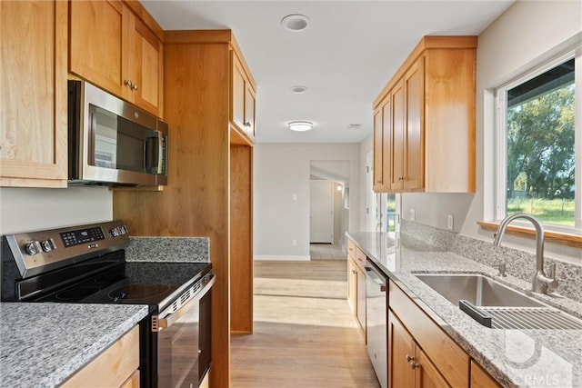 kitchen with stainless steel appliances, light stone countertops, a sink, and light wood finished floors