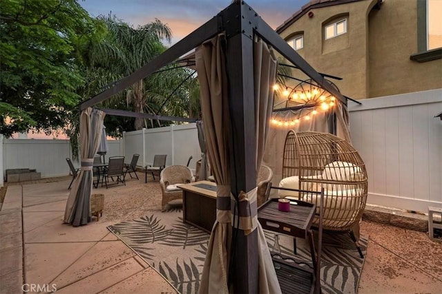 patio terrace at dusk featuring a fireplace, outdoor dining space, and a fenced backyard