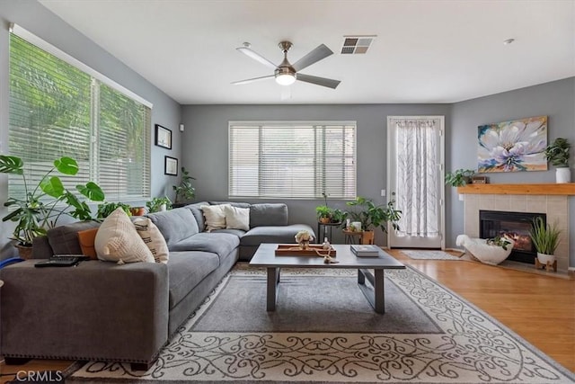 living area featuring a ceiling fan, visible vents, wood finished floors, and a fireplace