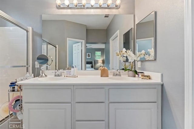 ensuite bathroom with visible vents, double vanity, a shower with door, connected bathroom, and a sink