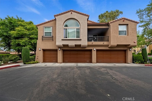 view of front of property featuring an attached garage, stucco siding, a balcony, and a tile roof
