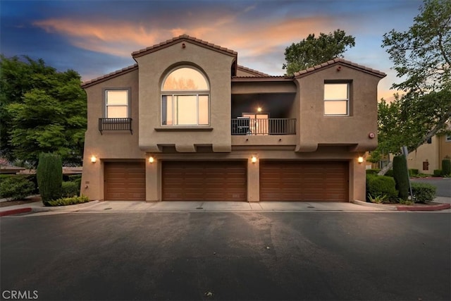 mediterranean / spanish-style house featuring a garage, stucco siding, and a balcony