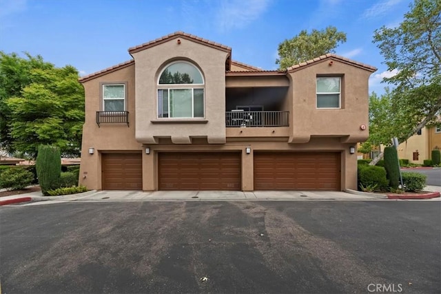 view of front of property featuring a tile roof, a garage, stucco siding, a balcony, and driveway