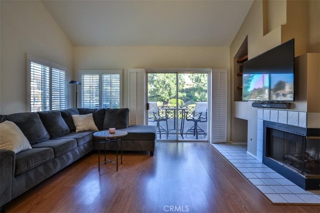 living area with a healthy amount of sunlight, high vaulted ceiling, wood finished floors, and a tile fireplace