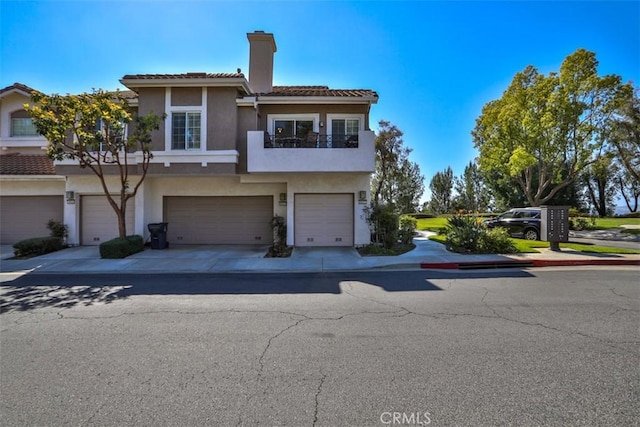 view of front of home with a garage, stucco siding, a chimney, a tiled roof, and driveway